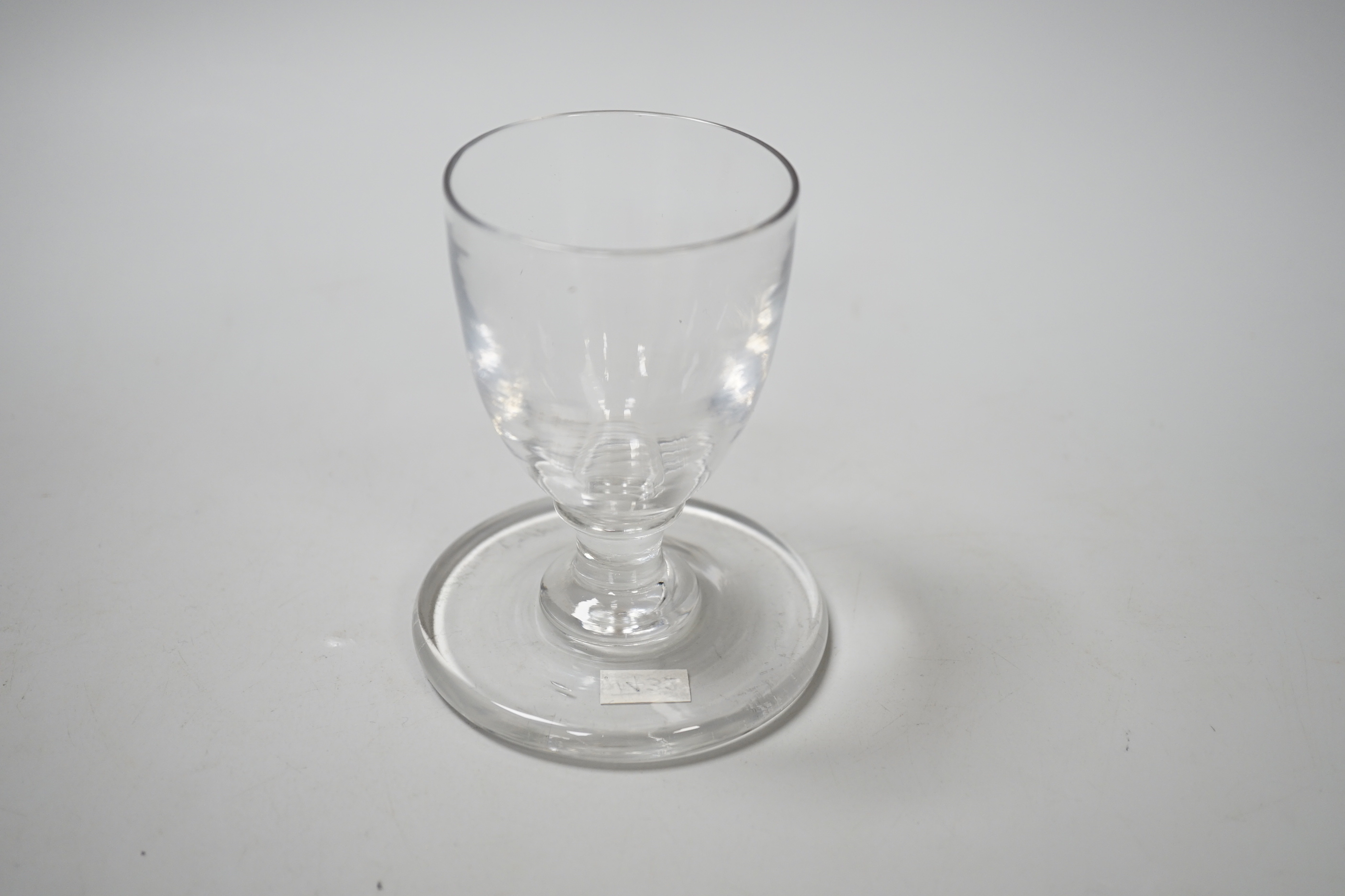 An English lead crystal ships’ dram, c1790-1800, the bowl, which is heavily striated, is of rounded funnel form on a capstan stem, with a very wide and heavy firing foot, 9.9cm high